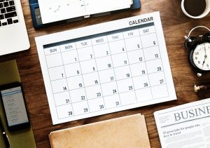 A calendar page on a desk, near papers, a tablet and a notebook. - Just what you'll need to plan the things to do after the move.