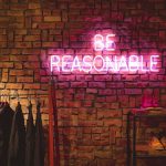 A wall with a purple neon sign saying 'Be reasonable'.
