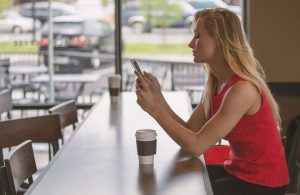 A woman holding a phone in a coffee shop, searching for reusable packing supplies.