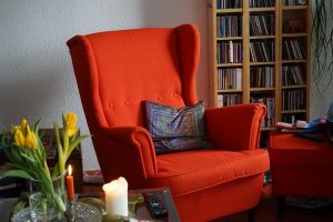 an orange armchair with a cushion on it, next to the table with candles and flowers