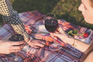 two people sitting on a blanket on grass, drinking wine